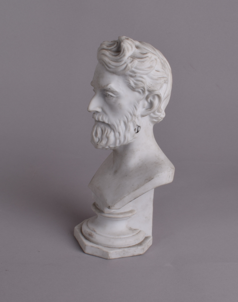 Liten byste av mann med skjegg på åttekantet sokkel.