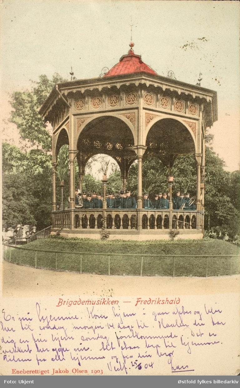 Postkort, kolorert lystrykk av paviljong i Halden der Brigademusikken spiller, 1903.