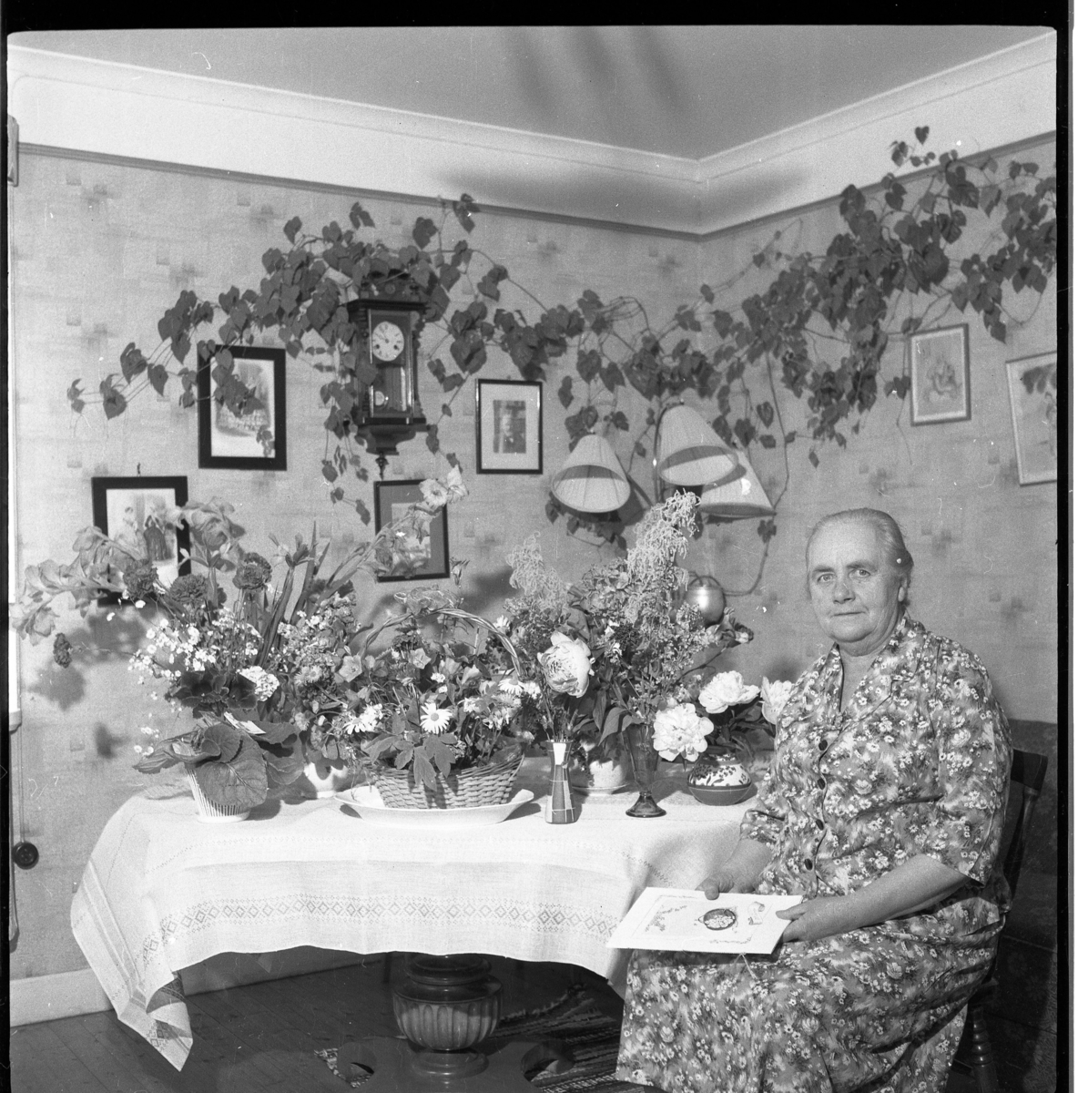 Ester Palm sitter vid ett bord fullt av blommor, förmodligen en högtidsdag.