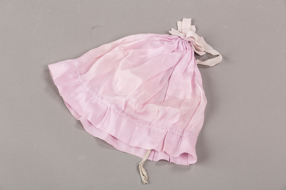 Hetten er rynket sammen i toppen og har rosett av silkebånd som pynt. Løpegang med strikk.