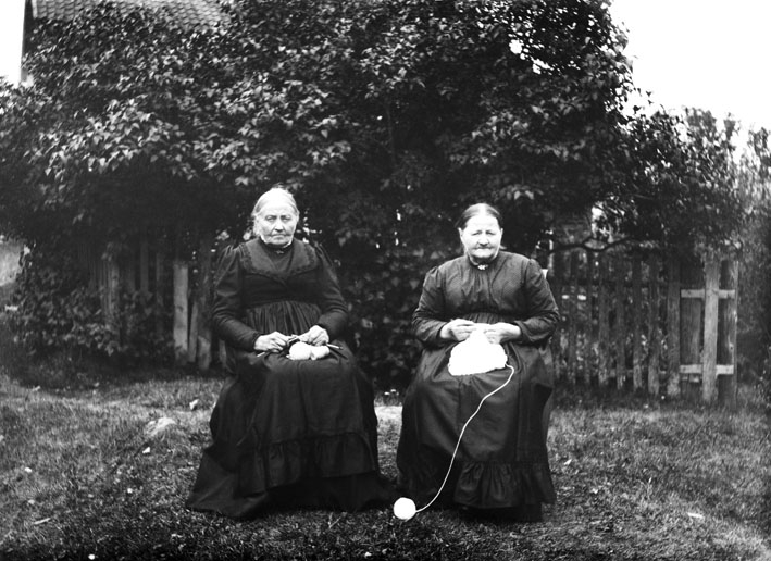 To kvinner med strikketøy, sitter ute i hagen