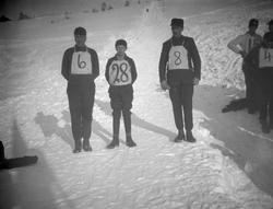 3 deltagere i hopprenn står i bakken uten ski, men med numme