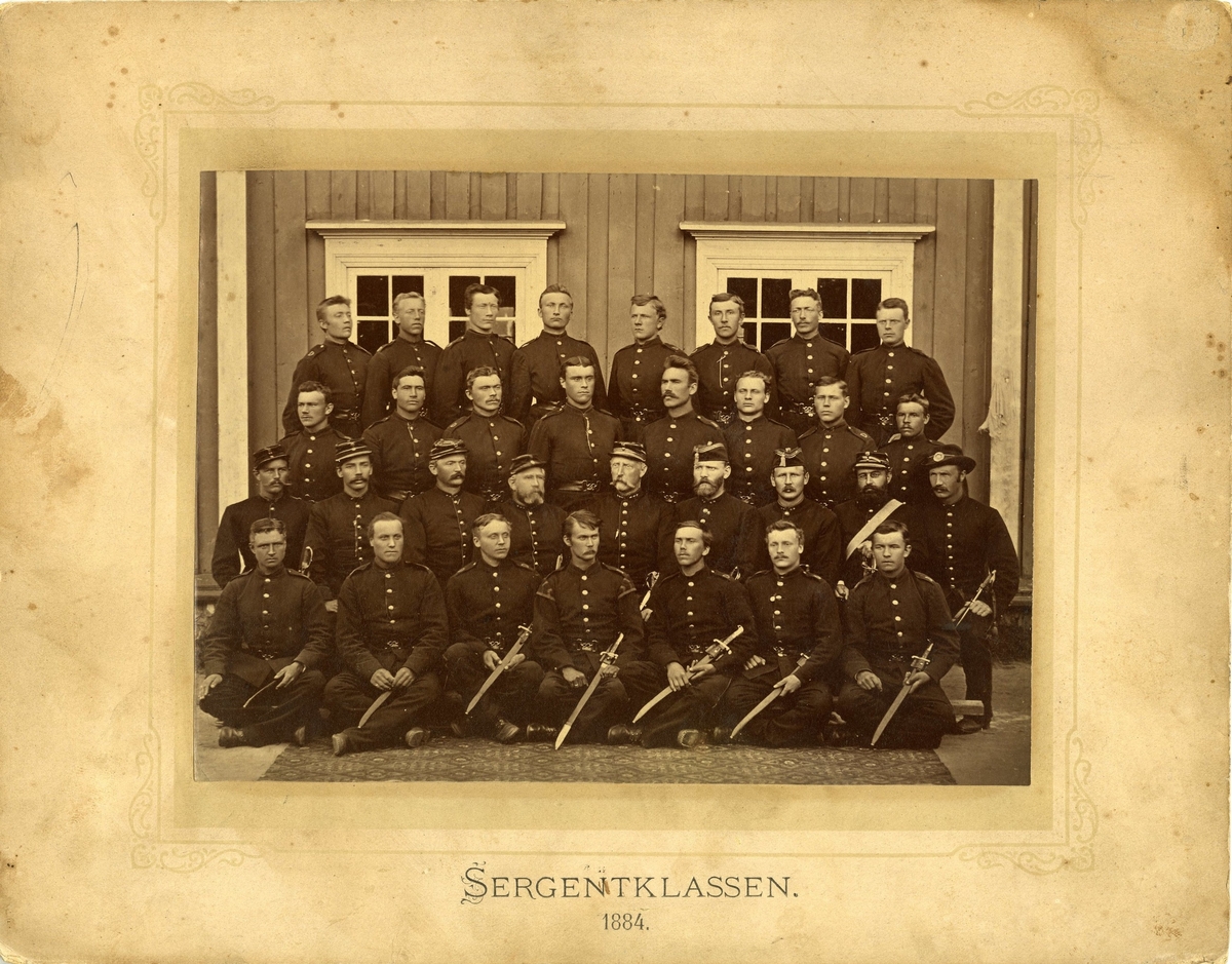 Gruppebilde av sergentklasse ifra 1884 iført uniform og paradesverd.
Navn bak på bildet. Det er en musiker på bildet. Første rekke i midten med "salereder"-Øverlie.