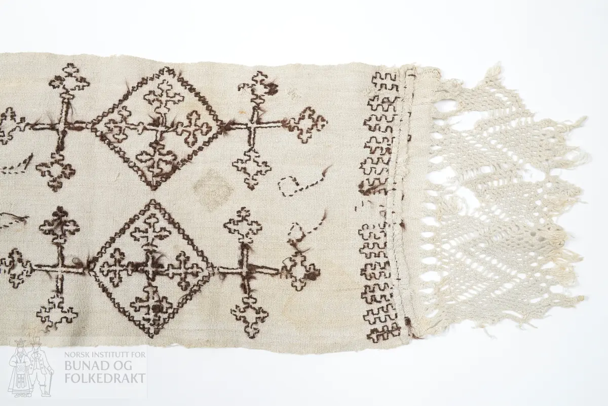 Er usikker på bruken av tekstilen. Kan ha vore sendingsplagg, hovudklut eller bårekross?
Av grov mjuk ubleika linlerret. Jare i båe langsidene. Broderi med holbeinsting med sauebrunt ullgarn. Båe endane har påsydd eit stykkje av liknande linkvalitet, der efsingane er knytt i firflettingsteknikk. Initialane MKD og årstalet 1799.