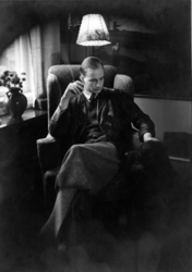 Niels Aall (1911 - 1982) sitter i stol og klapper hund

Inte