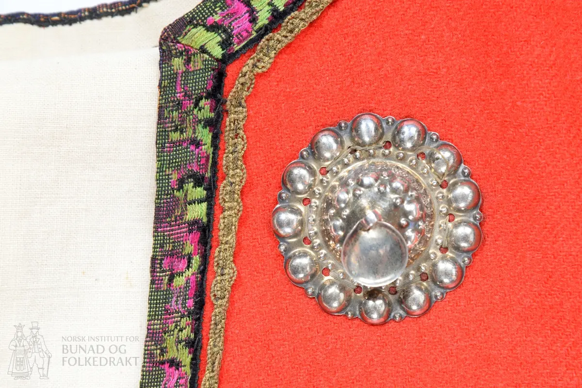 Liv sauma av raud ullkypert, lett valka. Fora med ubleika bomullslerret.
Ermhole, rundt hals og opning framme er kanta med blomstermønstra fleirfarga fløyelsband med svært avslitt fløyel. Innanfor kantingar er det påsett eit smalt metallband.
Etter framkantane er det påsett 3 borer på kvar side, dei to øverste litt breiare enn dei fire nederste, alle har eit skåleforma lauv festa i midten. På framsida av den kurva delen er det fem ulike stempel: 63 i eit sirkelforma stempel, truleg årstalsstempel. Månadsstempel: 6 over M i rektangelforma stempel. Mesterstempel i bølgeforma ramme LAR, Lorentz Christopher Angel Reimers, fekk borgarskap i Bergen i 1832. Lødighetsstempel 13 1/3. Trapesforma stempel med 7 prikkar, Bergens bystempel.
Lukking framme med to metallhekter på kvar side.
Heile livet er sauma på maskin. Kanting er sauma for hand. 
Livet sauma på stakken for hand. 
Stakken er av heimevove ullerret, blåsvart. Splittopning midt framme. Samansett av 5 rette høgder med jare i begge sider, alle høgder. Faldelagt oppe med eit glatt felt framme mot splitt. Høgdene er sauma saman med maskin. 
Nedkant: 3 svarte smale sillkefløyelsband, nedanfor dei eit påsett stoffstykke av svart bomullsfløyel. Dette stoffet er ein hengefald, ikkje sauma fast i nedkant.
Nedkanten er skonna på innsida med eit lerretsvove mohairstoff av mørk grøn farge. Sauma på med maskin. I nedkant av skonninga er det påsett eit blåsvart kosteband sauma på for hand.
Kanten på linninga er av svart bomullssateng. Er bretta dobbelt og sauma på for hand på begge sider