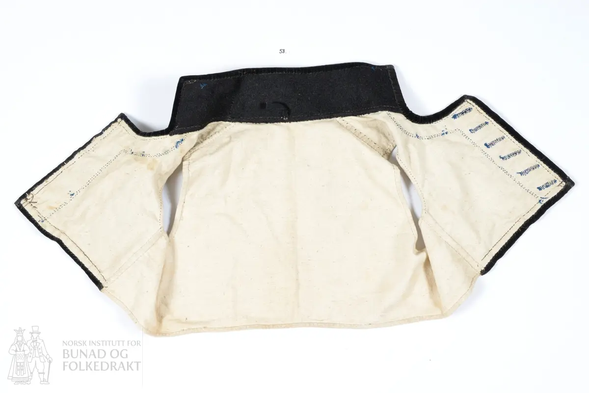 Vest, sauma av silkedroguet. Blå satengbotn med rosa flotterande trådar og innvove små blomster i ulike fargar. Framkant, krage og nedkant er påsydd ein smal svart kant av bomullsfløyel. Innanfor denne i framkant og krage er det påsydd eit breitt stykkje svart tynn fast klede. Denne er klipt med taggar etter sårkanten, pryda med tre tette konturstingsrader med blå ulltråd. 
Kragen er fora med tjukk brunsvart vadmål, sydd med to langsgåande avstivande stikningar. Ryggen er ufora, sauma av litt grov bomullslerret. 
Same type for i framstykkja. 
I ermholet på framstykkjet er foret bretta dobbelt rundt på framsida, og sydd ned med små javne faldesting. Sidesaumane er drage eit godt stykkje inn på kvart framstykkje. 
Eine framkanten har påsydd 6 stk skråstilte knapphol sauma av same type blå ulltråd. Merkjer etter knappefeste gjennom fløyelskanten på andre framstykkjet. 
I sidesaumen er hovudstoff framstykkje og ryggfor sydd saman med attersting, deretter er for framstykkjet bretta inn og sydd ned 1 cm bak den fyrste saumen, med faldesting som syner som prikk på retta.