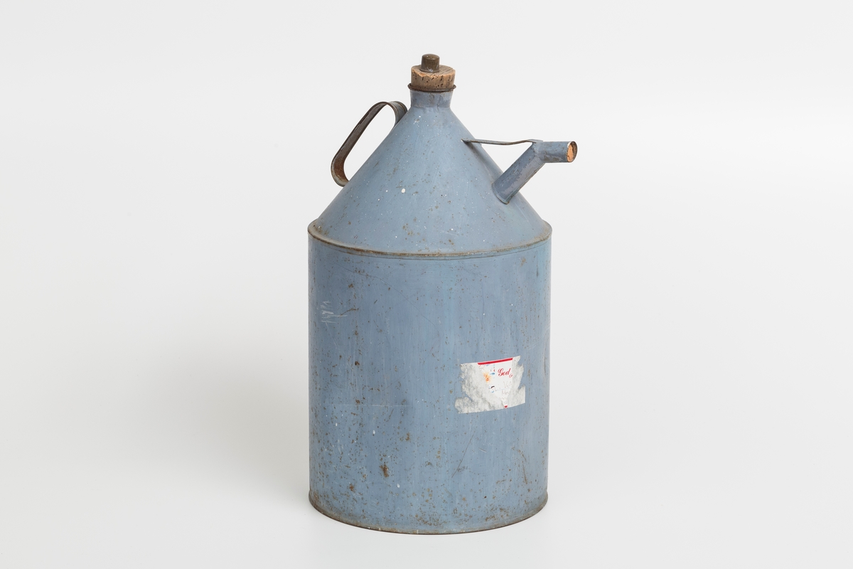 Kanne i sink, blå. Korket i tuten og korklokk med plast. Har håndtak og helletut. Kannen har påklistret god jul merkelapp med navn. Delvis avrevet.