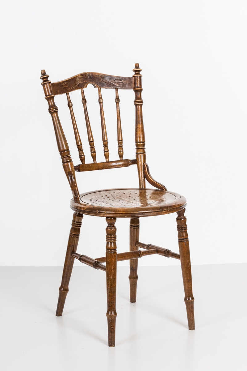 Stol i lakket treverk. Rundt stolsete med hullemønster. Rygg som er svakt buet med spiler og mønster. Dreide ben og spiler i rygg.