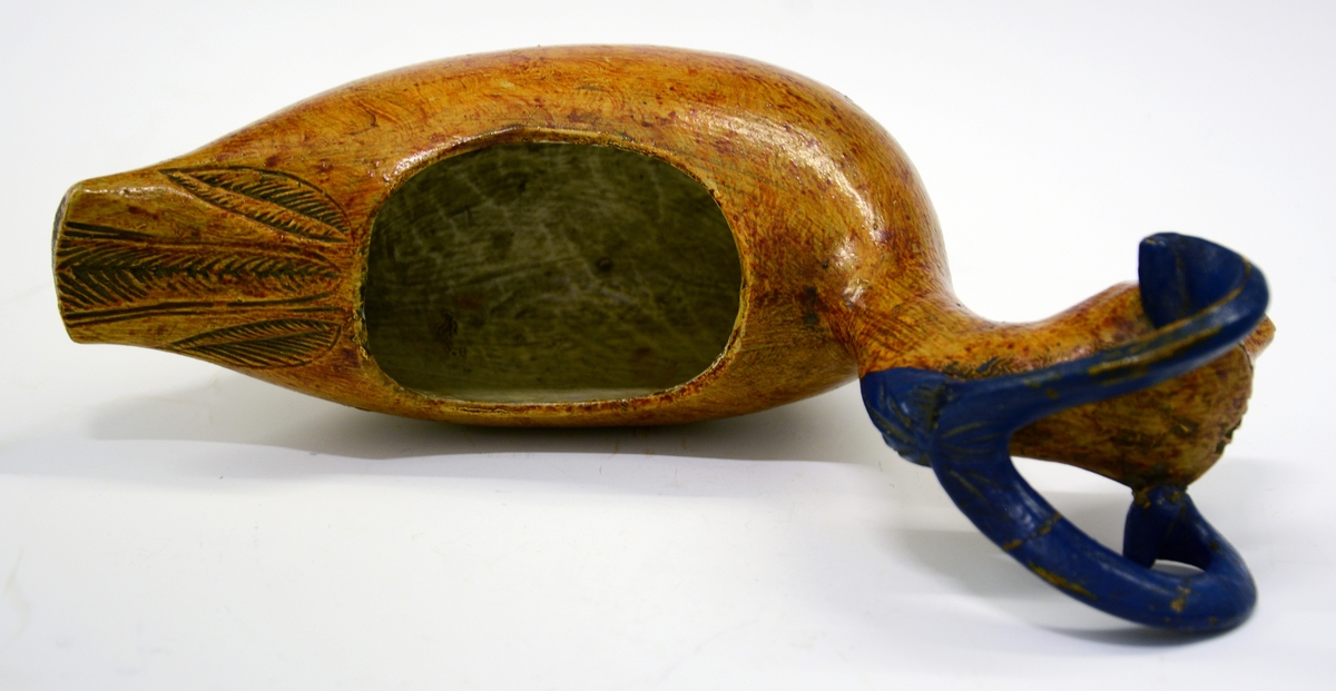 Kane. Fra protokollen: Kane, saak. "ølbøkaar", av træ. Kroppen nærmest mindende om gris + and, med 4 avstumpede ben og avstumpet hale. Hovedet bærer 2 foroverbøiede, fritliggende væderhorn (værhorn), som med sin forreste krumning hviler paa kjæven; hovedet forøvrigt væderlignende. Sen maling, kirketræsfarvet krop, blaa horn, hvit inside.