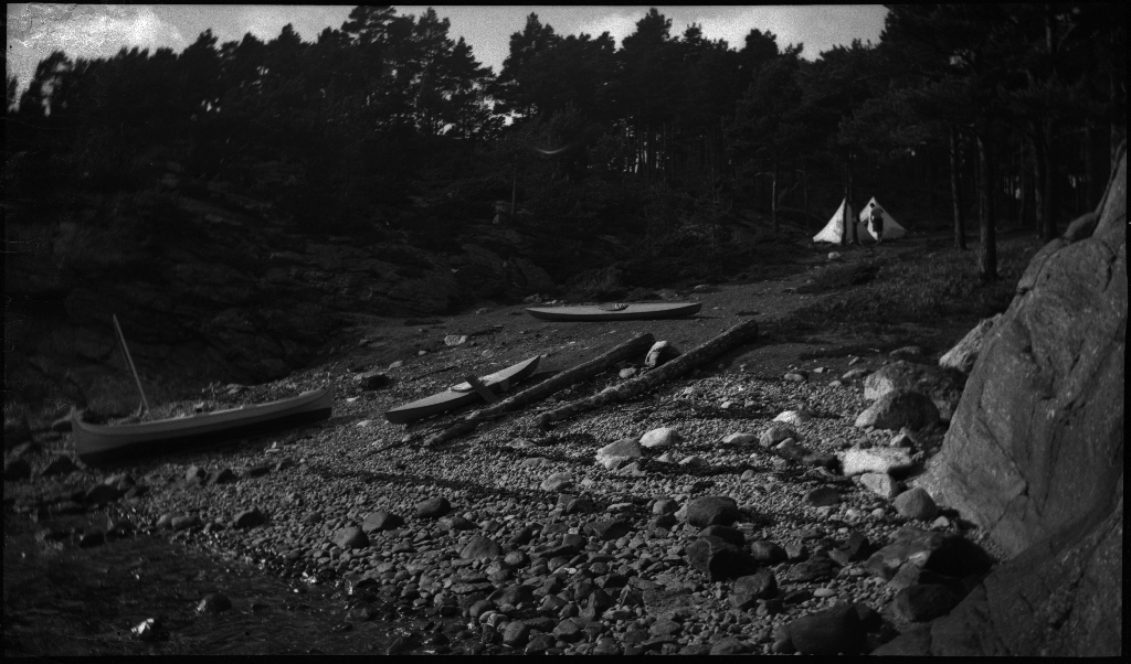 Fire unge menn på tur med nordlandsbåten og kajakker til Idse, ved innseilingen til Høgsfjorden. De har satt opp to telt og slapper av med blant annet kikkert og å stå på hendene. På bilde 14 er de ute med seil på nordlandsbåten.