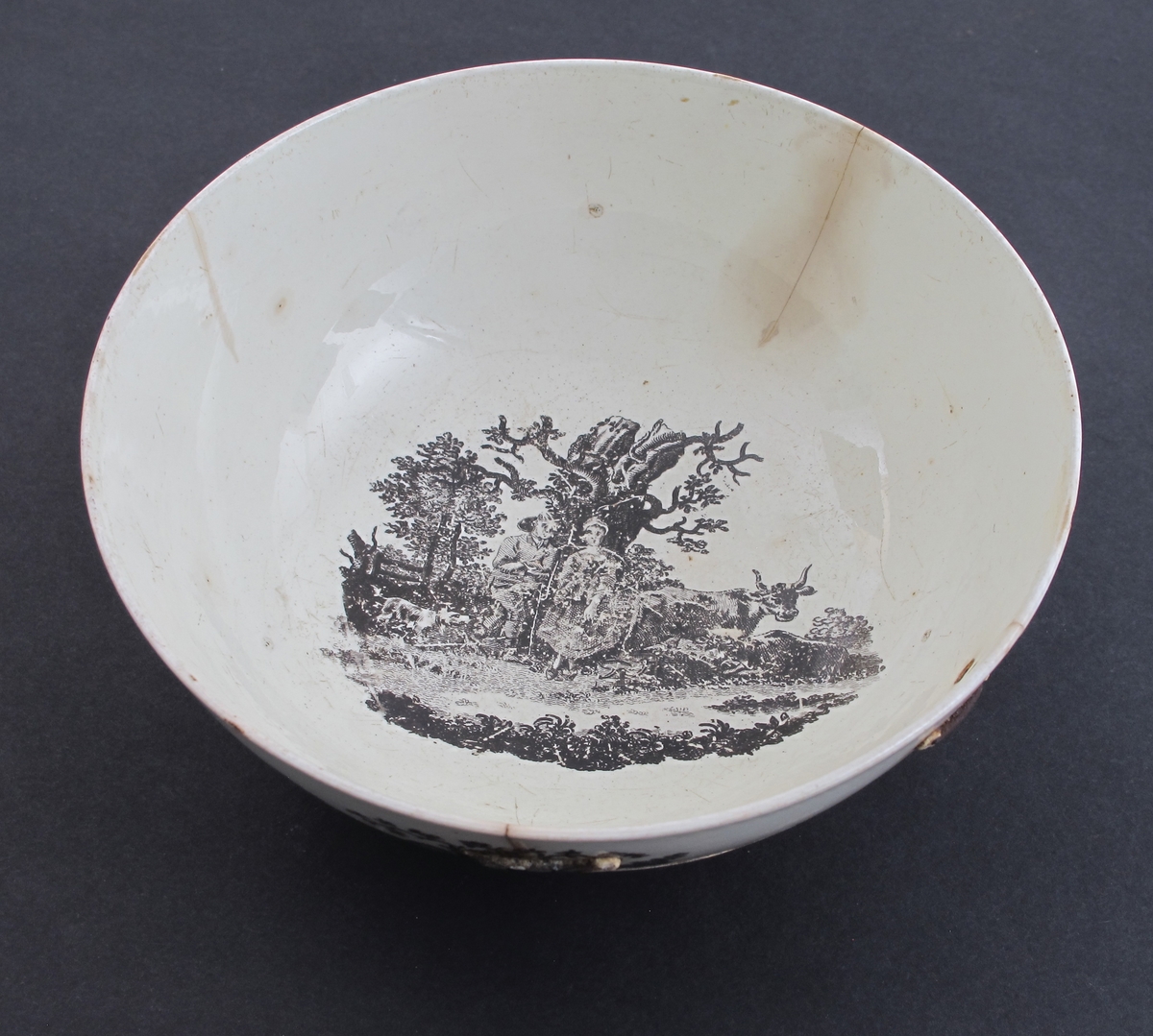 rundt siden 4 bonderomantiske landskaper: Gjeter og budeie  m. ku, Ku, der drikker i et vann; båt, vann og vind mølle;  Bonde der vasser over vann mot bondegård med sine to kuer; Beitende ku m. kalv, spaserende personer,  samt flod og hus i  bakgrunnen; innvendig i bunnen den  forelskede budeie  med sin gjeter i noe forstørret målestokk;