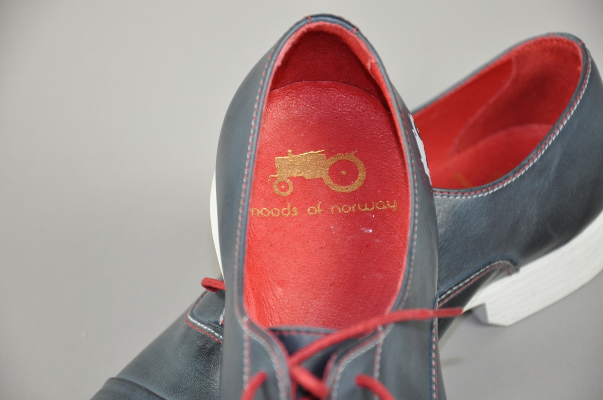Et par blå skinn herresko i str.44,røde skolisser,røde og hvite sømmer .
Traktor-logoen påtrykt i hvitt på begge skoene.