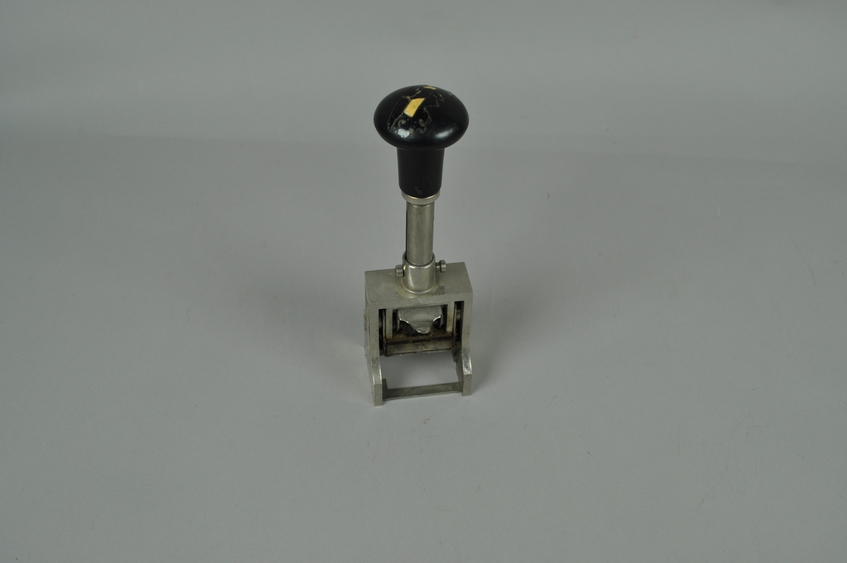 Stativdatostempel med håndtak. Stativet er i metall.