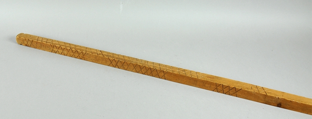 Målestokk av tre som er spiss i den ene enden. Det er inngravert mange kryss og punkter alle fire langsider med signaturer for hver rekke av merker.