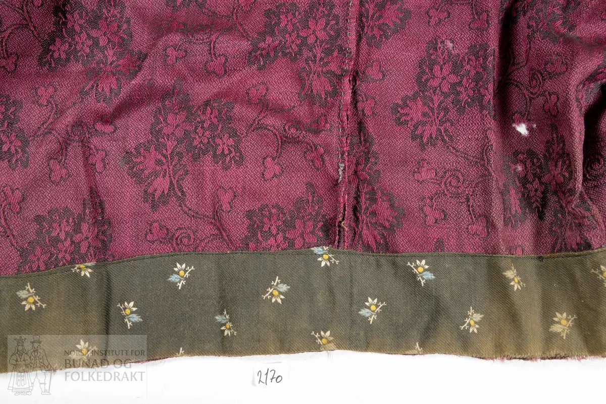 Brudestakk av mørk rosa og svart ulldamask. Av 3 høgder delvis sauma saman for hand og med maskin. Motfald midt framme, med eit breidt glatt parti midt framme. 3 breie legg på kvar side av motfalda. Midt bak eit 9 cm breidt rynka parti, med 2 breie legg på kvar side. 
Skonning og linning i trykt bomullskypert sauma på med maskin. Splitt midt bak lukkas med 1 par måla hetallhekter. I splitten møtes to jarekantar som er sauma ned med faldesting. På innsida av linninga er det påsauma to stoffhemper.
Stakken er bøtt i store stykkje både oppe ved linninga og i nedkant.