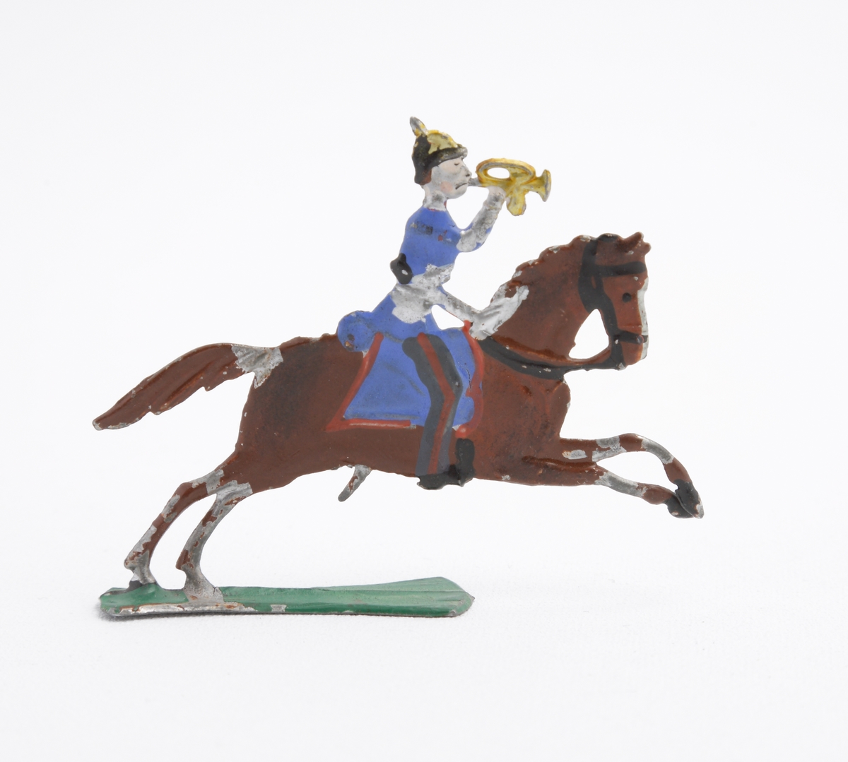 Ryttare till häst i blå uniform, trumpetare. Han är utrustad med koppel och pickelhuva. Sadeln är blå med röda kanter. Hästen brun på grön platta.
Inskrivet i huvudkatalog 1963.