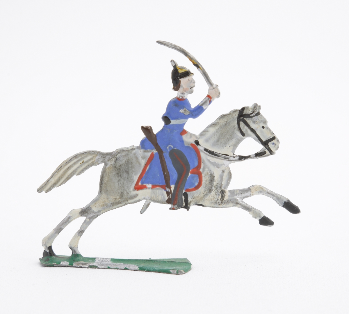 Ryttare till häst i blå uniform med dragen sabel. Han är även utrustad med koppel och pickelhuva. Sadeln är blå med röda kanter. Hästen vit på grön platta.
Inskrivet i huvudkatalog 1963.