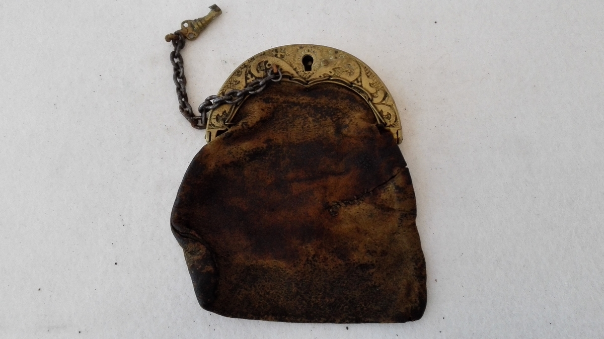 Form: Pung med lås av messing og nøkkel av jarnkjatting. Støypte ornament (ranke) på låset.