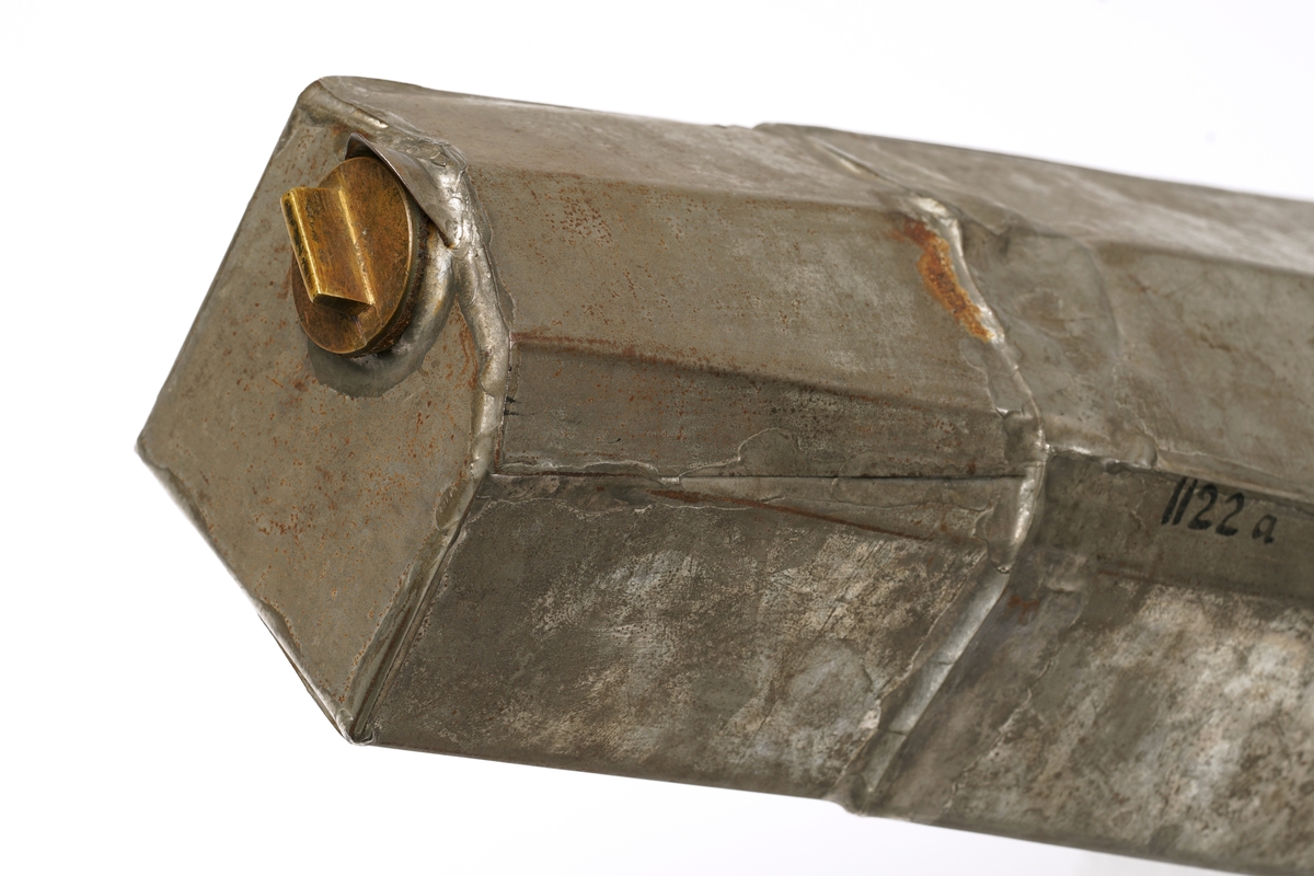 Svartlakkert fiolinkasse. Inni finnes en tank av metall, med tilpasset form etter innsiden av kassen.
I håndtaket på trekassen er det festet en nøkkel, som hører til låsen på kassen.