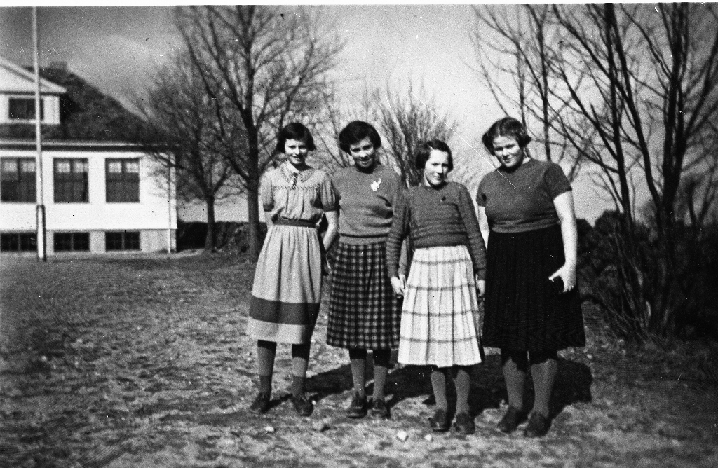Jentene i 5. klasse på Hognestad skule. F.v. Oddbjørg Serigstad g. Love (31.1.1939 - 4.3.2009), Åse Solfrid Oma g. Bore (21.6.1939 - ), Kari Emilie Hegdal g. Erland (5.9.1939 - 9.3.2018), Liv Tordis Hognestad (16.3.1939 - ), b. i Canada.. Skulebygningen bak til venstre. Den 5. jenta i klassen, Bolette Hognestad g. Ree (25.3.1939 - ), er fotograf.