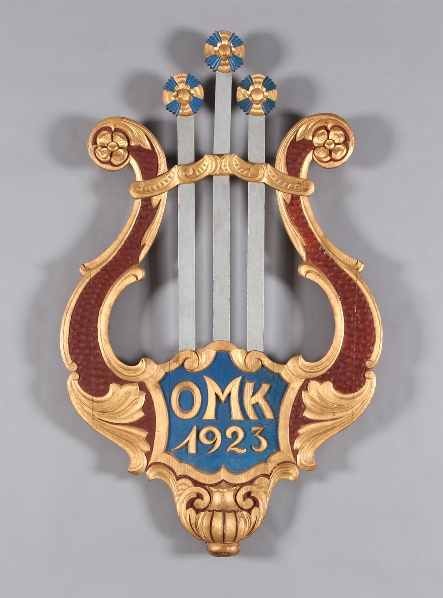 Gjenstanden er forma som ei lyre med stiliserte blomar. Lyre er eit strengeinstrument, sterkt knytta til den klassiske antikken, men bruka i Nord-Europa i vikingtida og tidlegare. Initialane OMK og skipingsår er plassert i motivet.