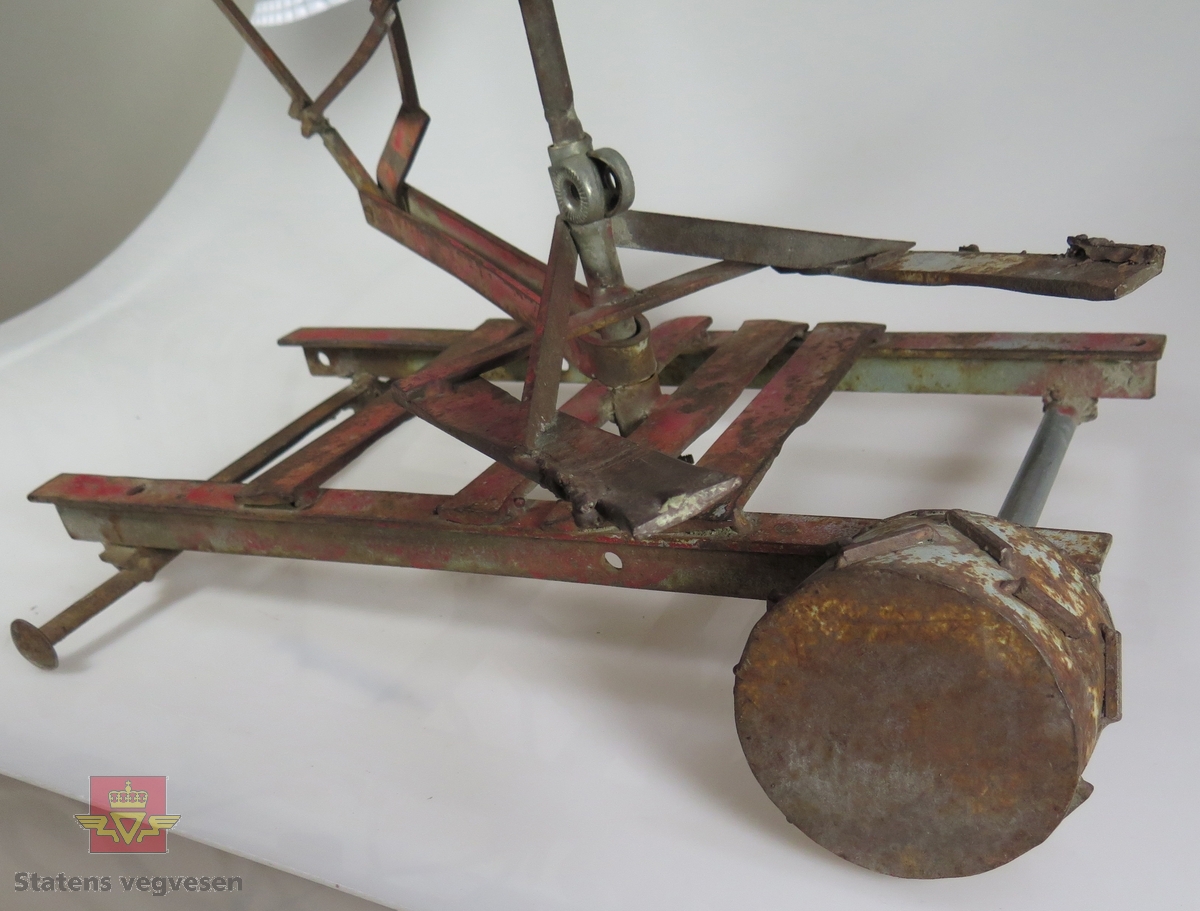 Gravemaskin lagd av metall, Skuffa styres av to spaker. Tre av hjulene og setet mangler. Rød.