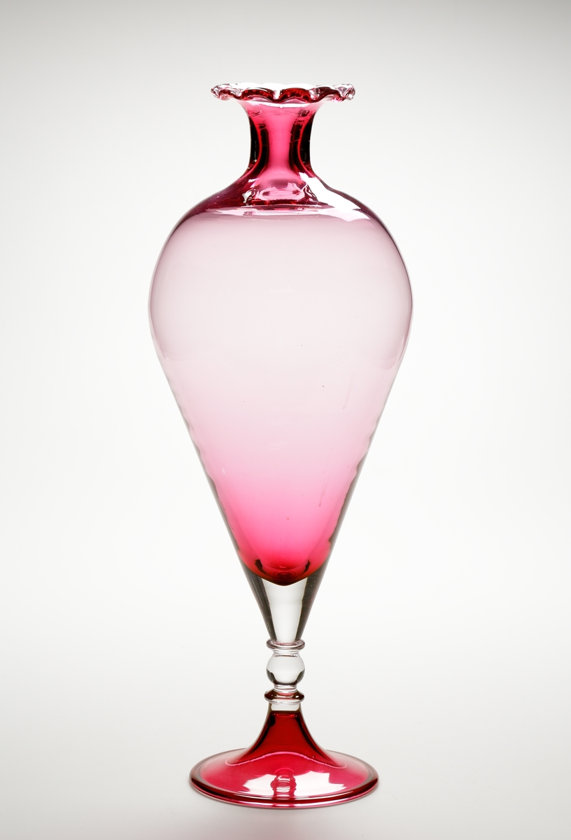 Vas eller pokal.
Stilen på glaset är gjord så att den ska se ålderdomlig ut.
Hög rosa vas/pokal som vidgar sig uppåt, och avslutas i en smal hals med utvikt mynning. Mynningen är veckad.
Benet är ofärgat och balusterformat.  
Foten rosa.