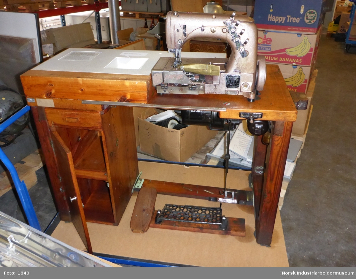 Brunlakkert arbeidsbenk med påmontert symaskin, elektromotor, diverse utstyr og en masse løse verktøy og annet til bruk i arbeid med tekstiler. Visstnok brukt for "påsying av halkrager og ribb (anfinger)"