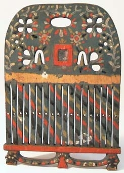 Bandvävsked av trä med genombrutet överstycke med en liten fyrkantig spegelglasbit inom röd ram på mitten. Bandgrinden är målad i gråblått med ornering i rött, gult, svart och vitt.
