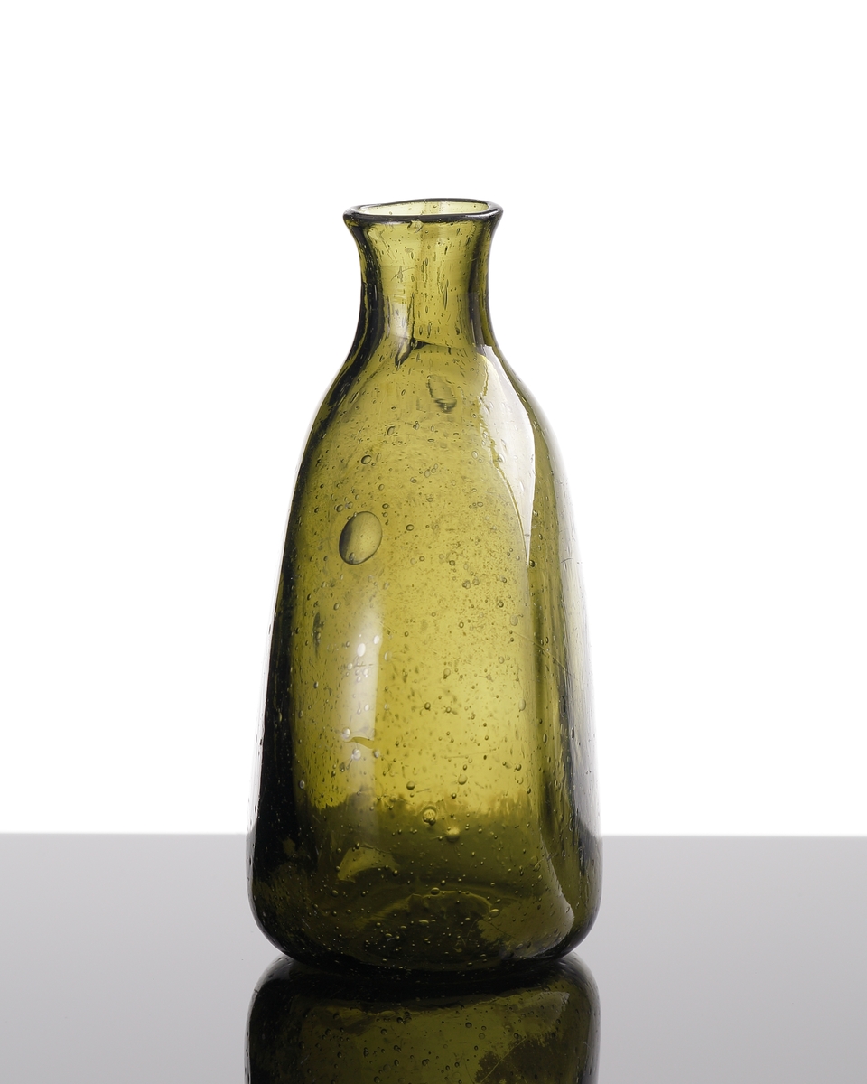 Brännvinsflaska av mindre modell, i mossgrönt glas.
Flaskan har plattade sidor.