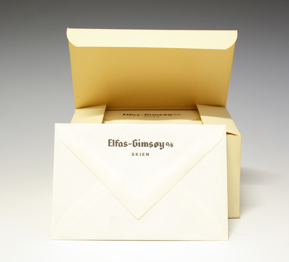 Rektangulær pappboks med vippelokk med ubrukte konvolutter. Konvoluttene har firmanavnet Elfas-Gimsøy A/S Skien på baksiden.