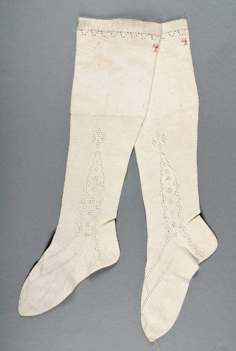 Ett par strumpor stickade av vitt bomullsgarn med mönsterbård och instickat årtal 1807 och initialerna D A.