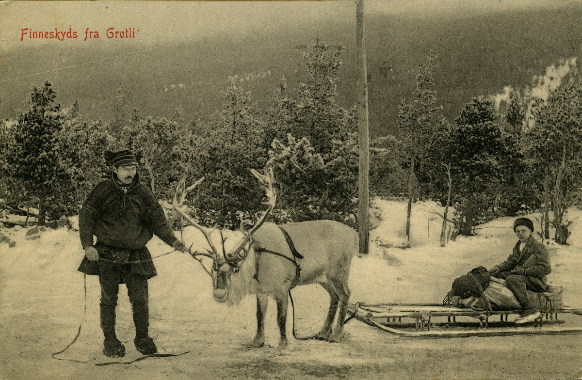 Postkort. Jule- og nyttårshilsen. Vintermotiv. En same holder et reinsdyr som dra en kjelke med en gutt med pakker. "Finneskyds fra Grotli". Stemplet 27.12.1920.