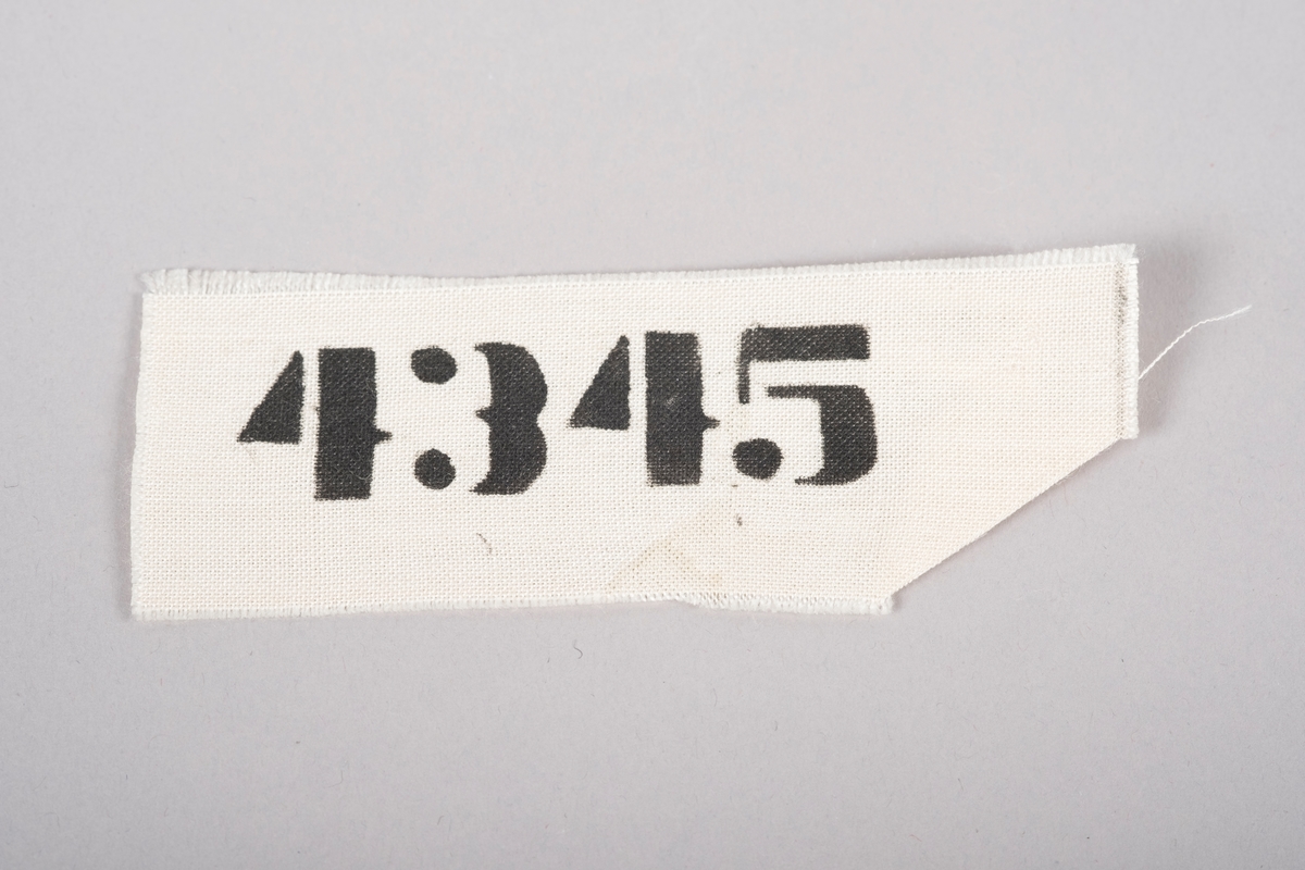 Fangenummer (4345) i svarte, trykte tall på hvitt vevet stoff.
