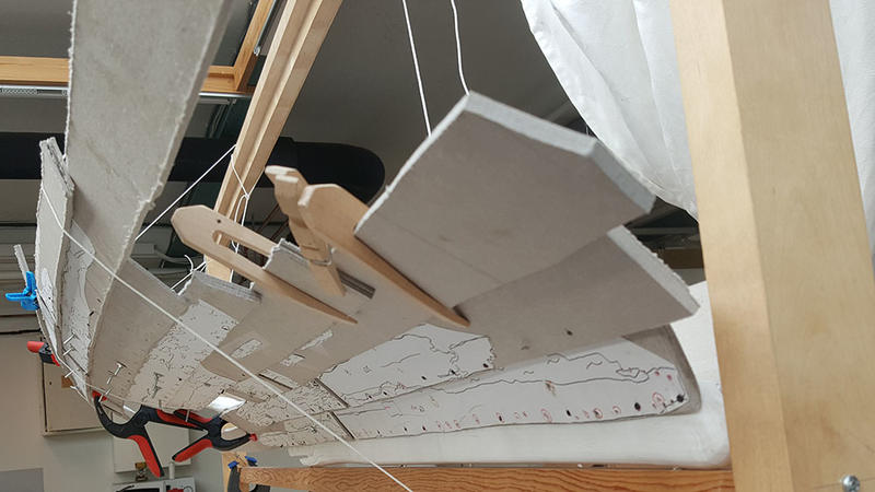 Modellen av Lovundbåten sett akter- og nedenfra. Bord i papp holdes på plass av klyper i tre og snører hengt opp i treramme.