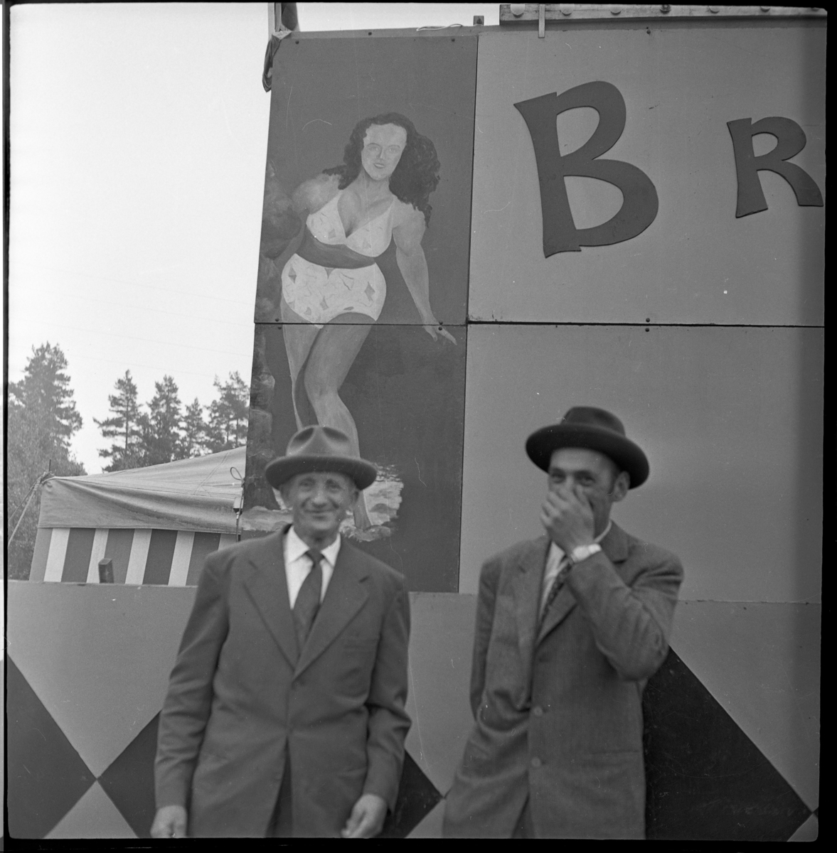 Marknad på Gränna torg. Två män framför skylt med målad kvinna i bikini. En av dem är Einar Karlsson.