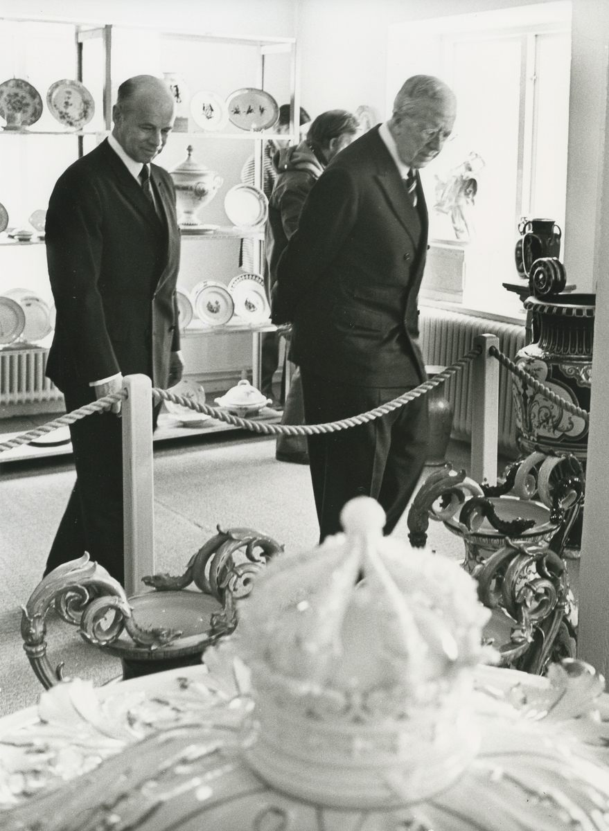 Kungligt besök på Gustavsbergs porslinsfabrik, sannolikt i Porslinsmuseet i Gula Husets Gamla kontorets kyrksal.
Personer: Kung Gustav VI  och VD Bo Broms