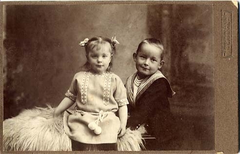 Kabinettsfotografi: barnen Margit och lill Olle Rogberg sittande respektive stående vid en skinnfäll.