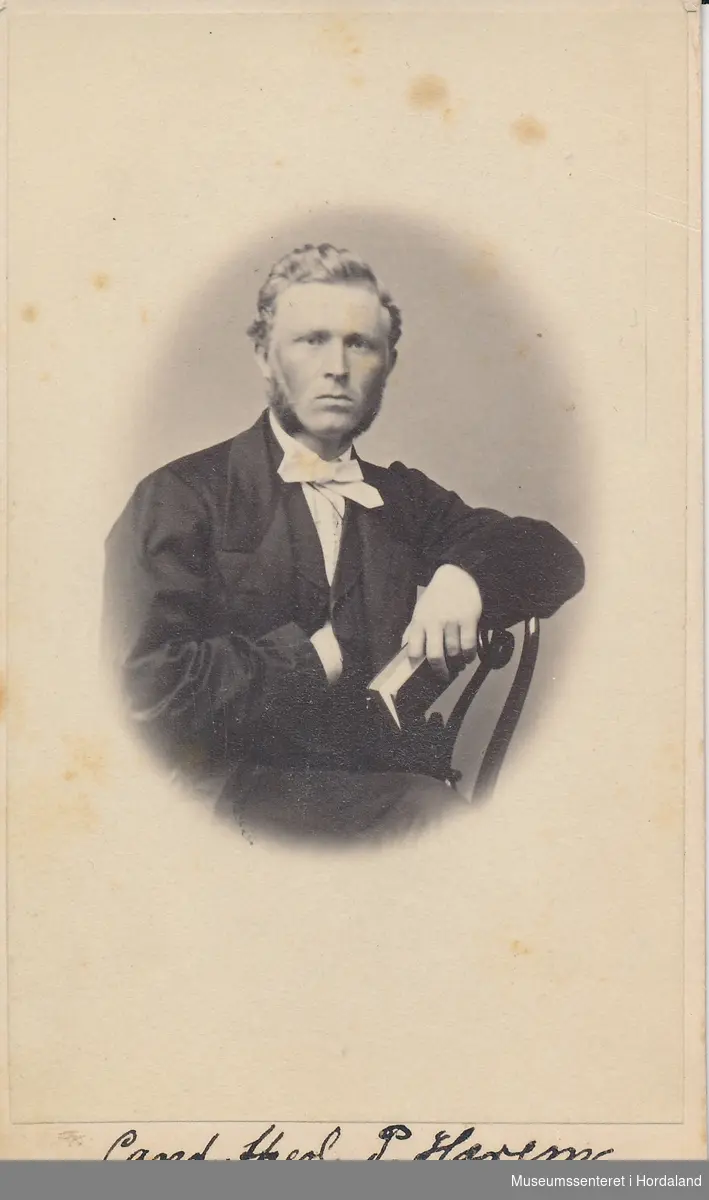 halvfigur fotografi av  ung mann med svart jakke, kvit skjorte med sløyfe og bok(?) i handen