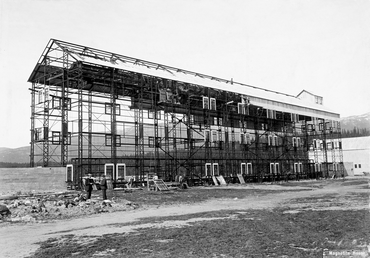 Magnetitthuset ved Dunderland Iron Ore Company Ltds anlegg ved Storforshei i Rana under oppførelse tidlig på 1900-tallet.  Bygningen var en høy, treetasjes stålkonstruksjon, der monteringa av vinduer, tak- og veggplater var påbegynt da bildet ble tatt.  Flere arbeidere ses på bygget.  I forgrunnen til venstre samtaler to funksjonærer. 

Dette fotografiet er tatt i samband med den industribygginga selskapet Dunderland Iron Ore Company Ltd. sto bak tidlig på 1900-tallet.  Selskapet ble organisert i 1902 med sikte på å utnytte seks malmfunn i Dunderlandsdalen gjennom magnetseparering av forholdsvis fattig, finknust malm og påfølgende produksjon av jernbriketter.  Produksjonen kom i gang i 1907, men den var ikke økonomisk bærekraftig og ble følgelig avviklet alt i 1908.  Virksomheten ble gjenopptatt seinere med annen teknologi.  En orientering om den tidlige fasen i virksomhetens historie finnes under fanen «Opplysninger». 