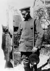 Hamarmannen Knut Emilsen (1876-1942), fotografert ved en 13 kilo tung og 90 centimeter lang ørret han tok i Mjøsa utenfor Snekkersvea på Nes (på vestsida av Furnesfjorden) den 2. juni 1925.  Emilsen hadde hengt storfisken i flaggstanga.  Sjøl sto han ved siden av, kledd i ei uniformsliknende jakke uten distinksjoner og med ei lue med blank skygge på hodet.  Med venstre hånd støttet han et «dreggsprøtt» - ei fiskestang med ei diger tresnelle, en redskapstype som ble brukt under dorging i Mjøsa.  Fotografiet er tydeligvis tatt i fiskerens egen hage.  Vi skimter stakittet mot nærmeste gate og bebyggelsen på motsatt side.  Knut Emilsen var født på en av husmannsplassene under garden Stor-Imerslund i Vang, men som voksen bodde han i Grønnegata på Hamar.  Han var bryggeriarbeider av yrke.
Mjøsørret. Mjøs-ørret. Hunderørret. Dreggeprøtt. Fiske. Sportsfisker. Sportsfiske. Dorging. Fangst.
