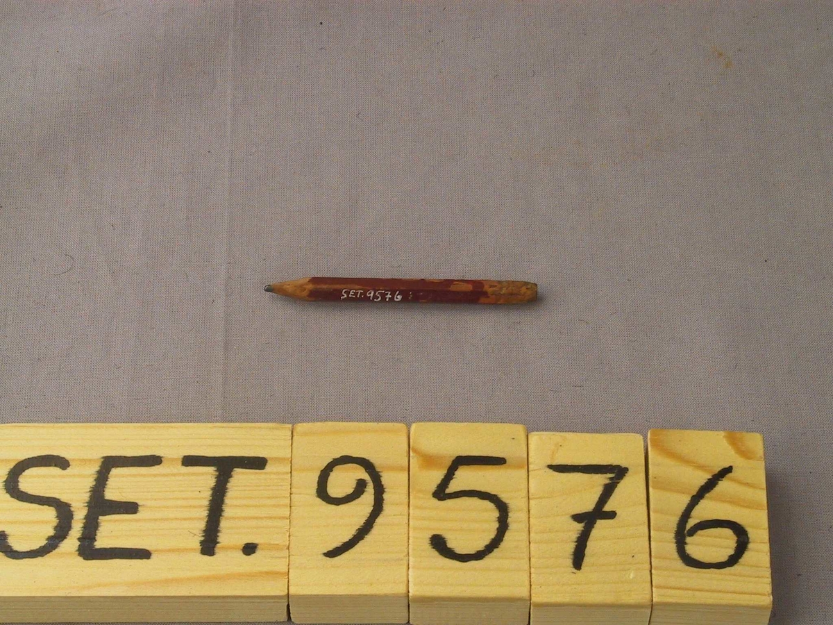 Vanleg blyantstubb med 6-kanta tverrsnitt, biten på i enden og kvesst med kniv. Det ser ut som bokstaven M er skoren inn. 

