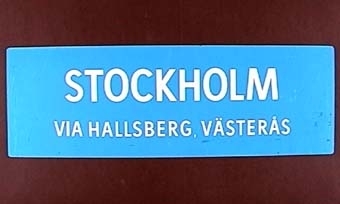 Rektangulär dubbelsidig plastskylt med vit text på blå botten:
"STOCKHOLM
VIA HALLSBERG, VÄSTERÅS".

Samma text på andra sidan.