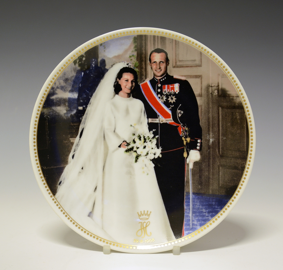 Platte med bryllupsbilde av Kronprins Harald og Kronprinsesse Sonja med monogram og bryllupsdato 29.08.1968. Gullstrek med prikket bord ytterst på fanen.