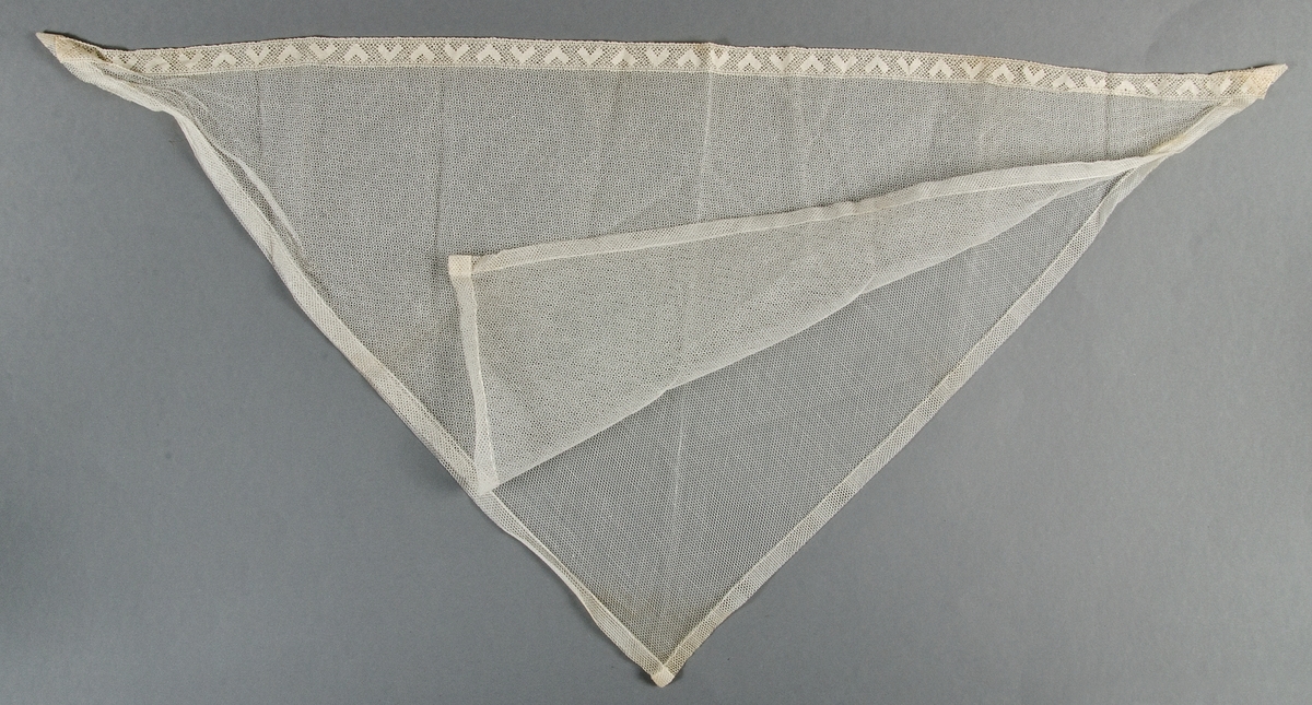 Schal av vitt tyll, dubbelt tyg med tyllspets i ena kanten.
Har använts på huvudet.