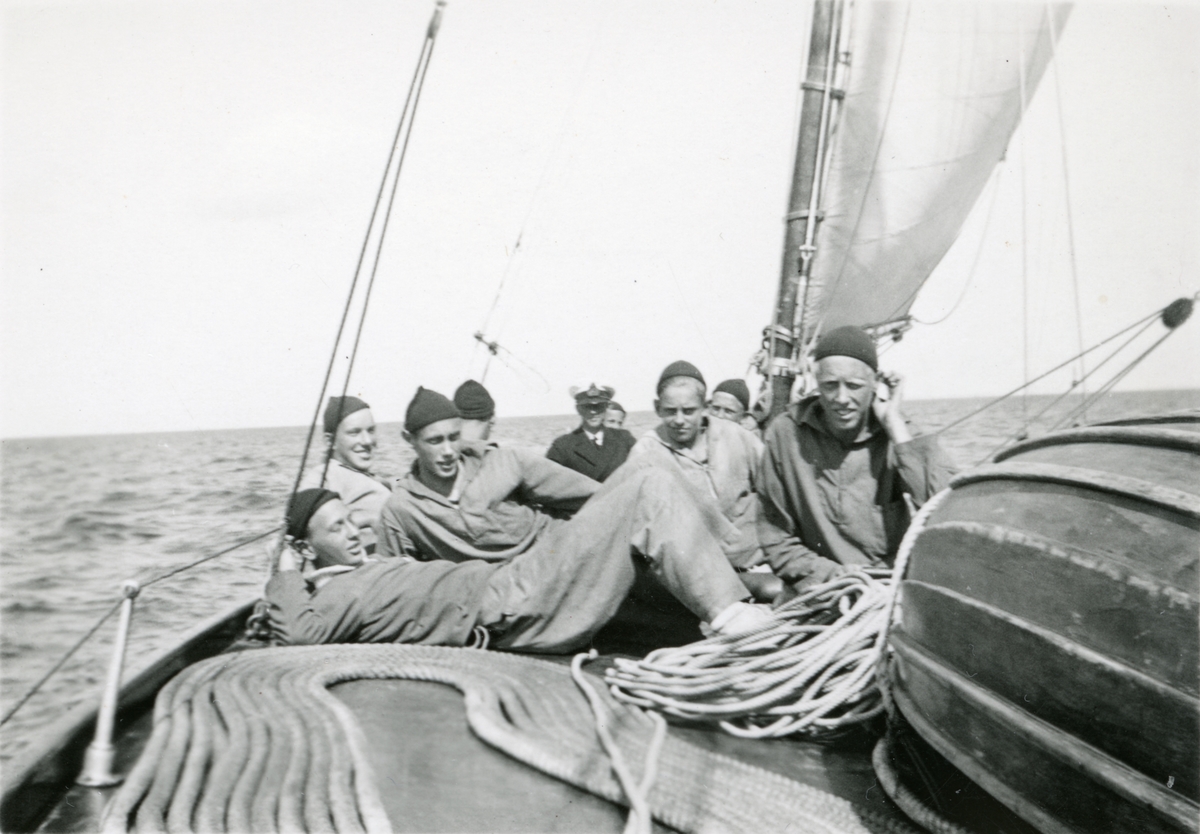 Unga män sitter på däck med kapten i bakgrunden.
