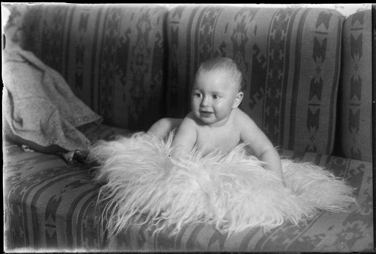 En bäbis ligger på en fäll i en soffa. I fotografens egna anteckningar står det "Fredrikssons pojke".