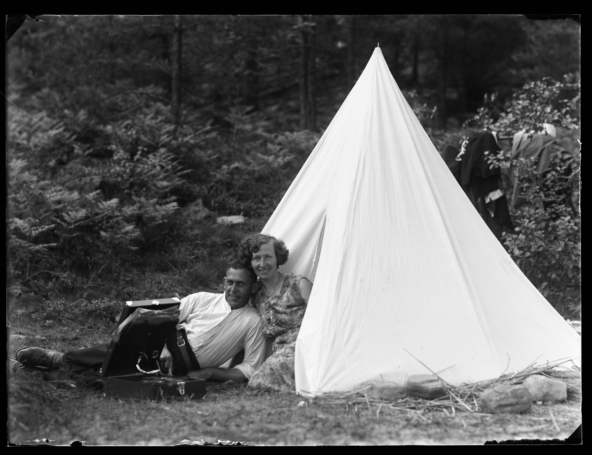 Hugo Larsson och Märta Karlsson fotograferade på Risö. Märta sitter i öppningen på ett tält medan Hugo ligger på gräset med en resegrammofon framför sig.