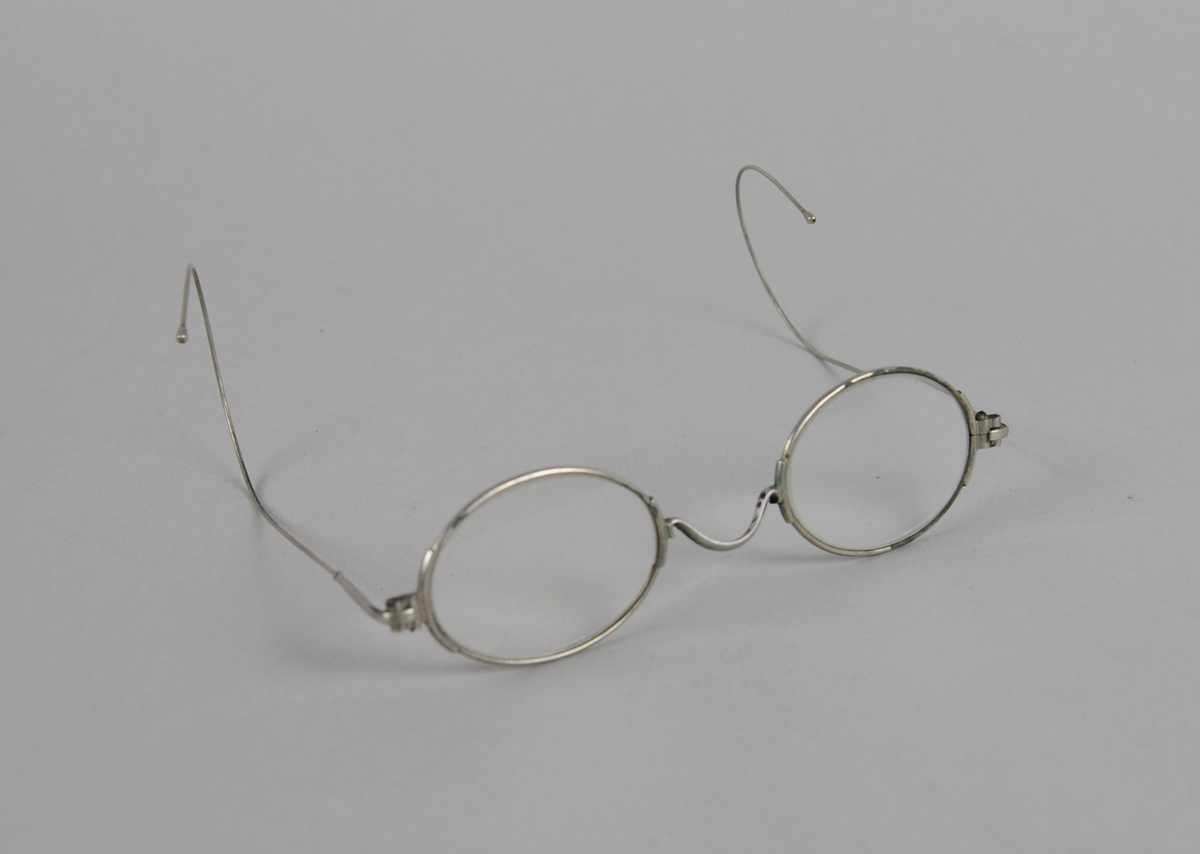 Ovale briller med metallinnfatning. Brillestengene er buet på endene.